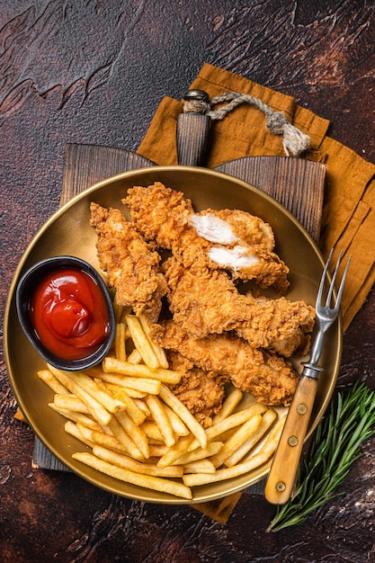 Fried Breaded chicken tender strips with french fries and tomato ketchup on a plate Dark backgrund Top view