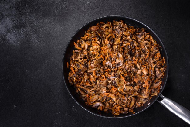 Fried champignons with carrots onions and spices in a pan against a dark concrete background