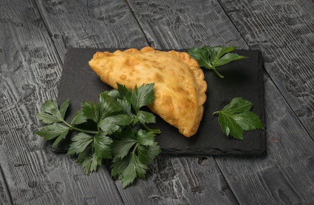 Fried cheburek on a board with spicy herbs