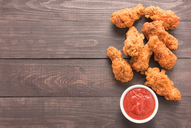 Fried chicken drumstick and ketchup on wooden background