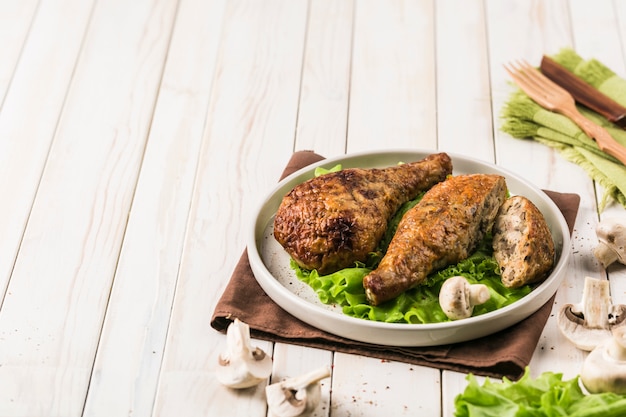 Fried chicken drumstick stuffed with mushrooms flat plate with lettuce leaf on light wood.