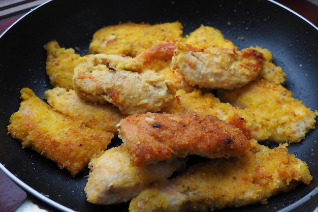 Fried chicken fillet in a black pan closeup Many pieces of fried chicken rolled in breadcrumbs Homemade quick recipes for cooking and body processing of meat products