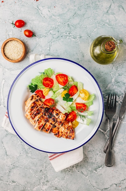 Fried chicken fillet and fresh vegetable salad of tomatoes over gray marble.