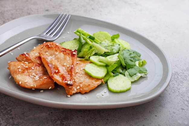 Fried chicken fillet in soy sauce on a plate decorated with sesame seeds and green salad.