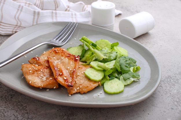 Fried chicken fillet in soy sauce on a plate decorated with sesame seeds and green salad.