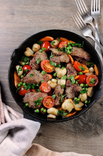 Fried chicken liver with vegetable side dish of tomatoes, carrots, mushrooms, peas in a pan