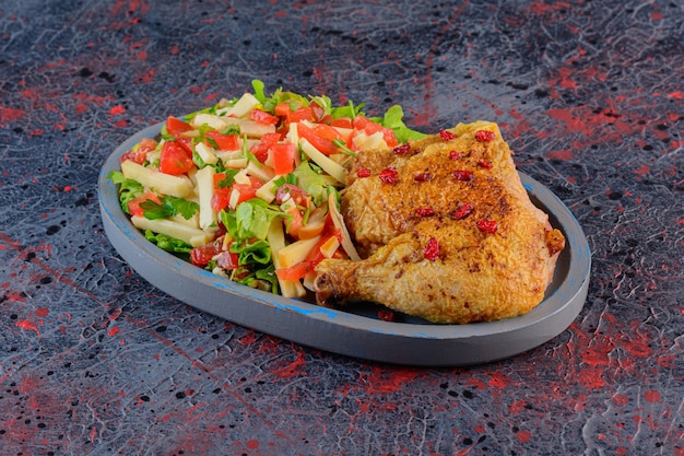 Fried chicken meat with mixed vegetable salad on a dark background.