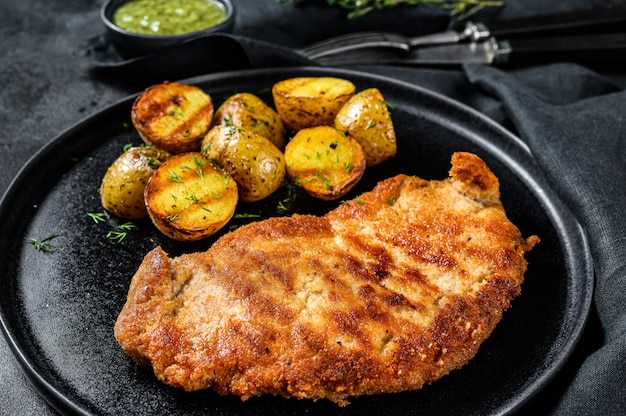 Fried Chicken schnitzel with baked potatoes. Black surface. Top view