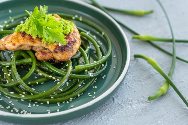 Fried chicken steak with garlic arrows and sesame seeds in green plate on gray concrete table