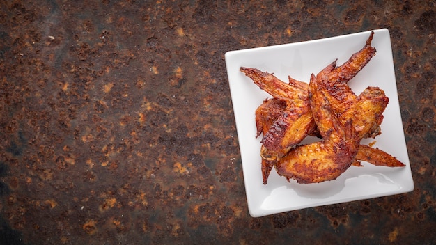 Fried chicken wings in white square ceramic plate on rusty texture background with copy space for text, top view, full HD ratio