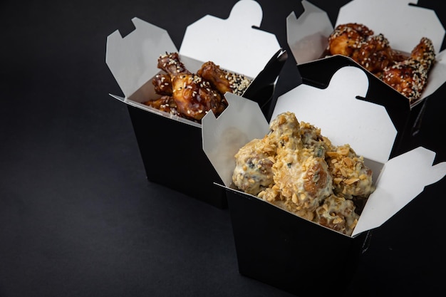 fried chicken wings with sauce and cheese in a delivery box on a black background