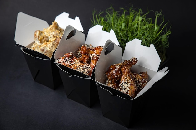 fried chicken wings with sauce and cheese in a delivery box on a black background