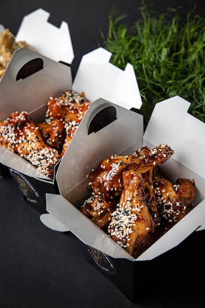 fried chicken wings with sauce and cheese in a delivery box on a black background