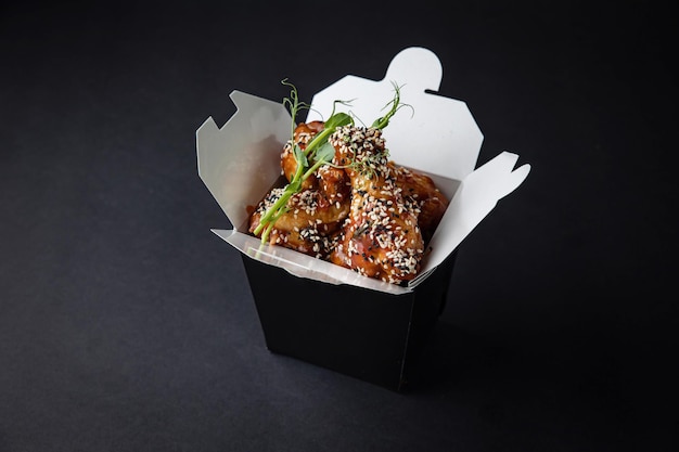 fried chicken wings with sauce and cheese in a delivery box on a black background