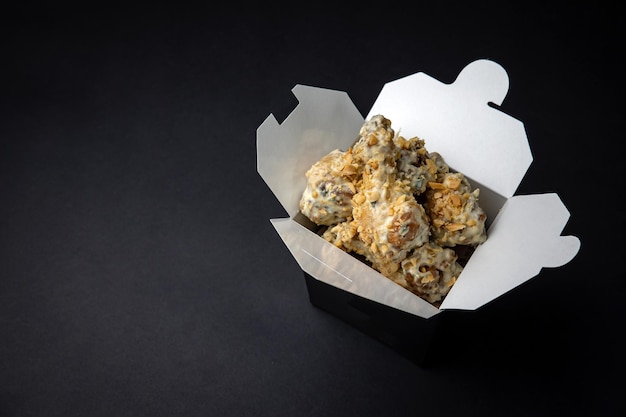 fried chicken wings with sauce and cheese in a delivery box on a black background