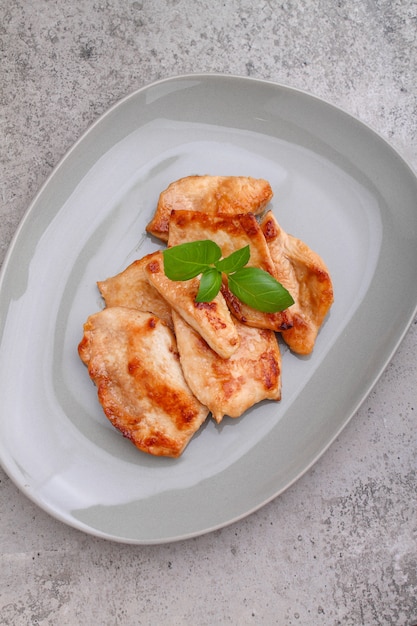 Fried chicken with soy sauce on a plate decorated with sesame seeds and basil, top view