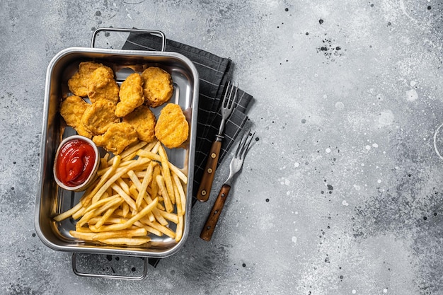 Fried crispy chicken nuggets with ketchup and French fries. Gray background. Top view. Copy space.