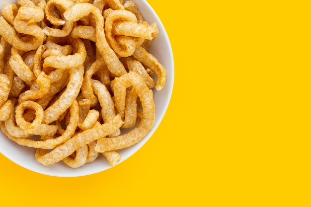 Fried crispy pork rinds in white plate on yellow background.