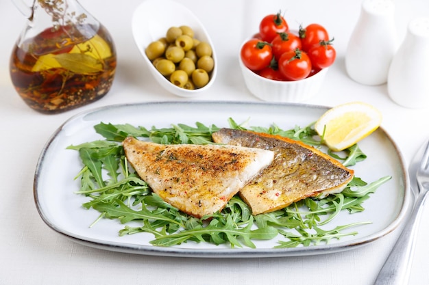 Fried dorado fillet with crispy skin Arugula cherry tomatoes olives lemon and olive oil Traditional Mediterranean dish White background Selective focus closeup