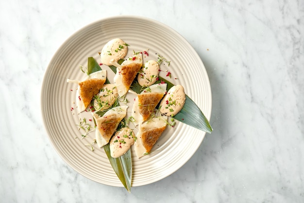 Fried dumplings or Japanese Gyoza in yellow sauce, cherry tomatoes and green peas, served in a white plate on a marble table. Pan-Asian cuisine. Restaurant food