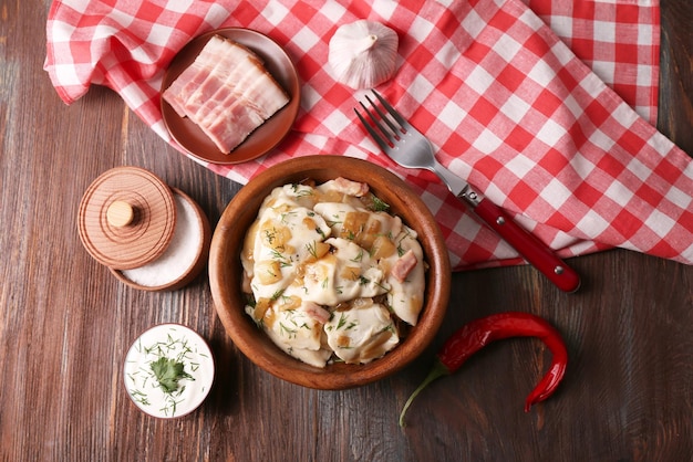 Fried dumplings with onion and bacon in frying pan on wooden table background