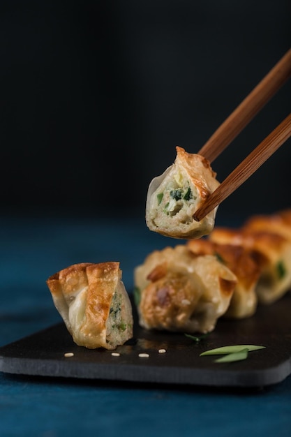 Fried dumplings with pork and greens on a black graphite board with chopsticks on a dark background Focus on the cut Korean food Closeup with a copy space for the text Vertical orientation