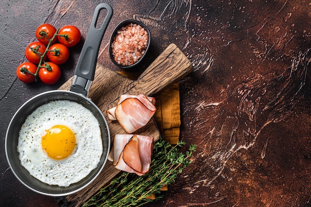 Fried egg in a frying pan with tomatoes and bacon. Black background. Top view. Copy space.