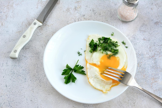 fried egg isolated on white plate with parsley, fork and knife, close-up