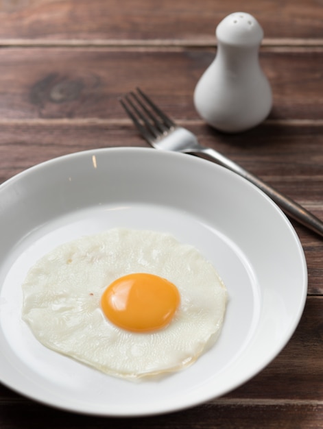 Fried egg in white plate with fork on wooden table