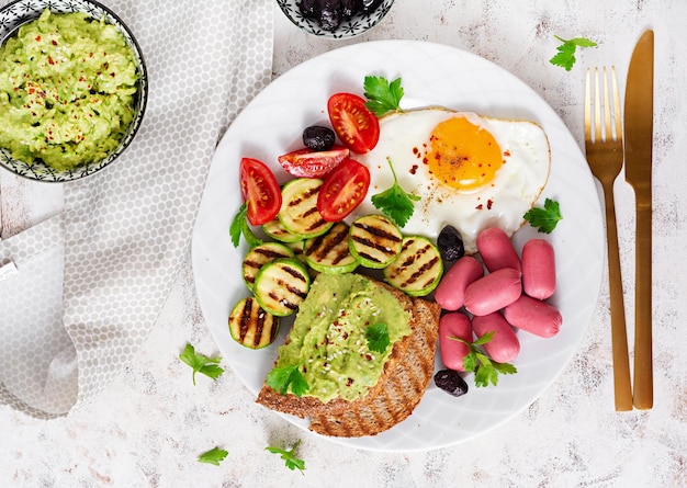 Fried egg with mini sausage tomatoes grilled zucchini black olives and toasts with guacamole English Breakfast Brunch Top view