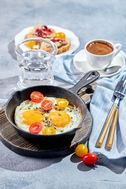 Fried eggs. Fried eggs from two eggs in cast-iron pan with cherry tomatoes and microgreens, toast and cup of coffee. Sunny morning breakfast concept