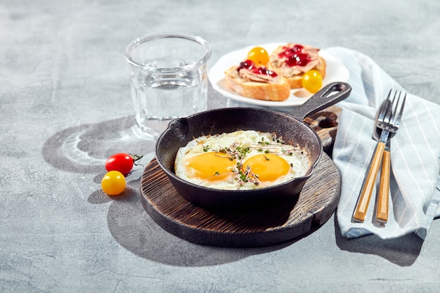 Fried eggs. Fried eggs from two eggs in cast-iron pan with cherry tomatoes and microgreens, toast. Sunny morning breakfast concept