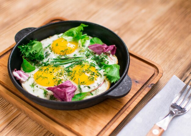 Fried eggs in a frying pan and greens