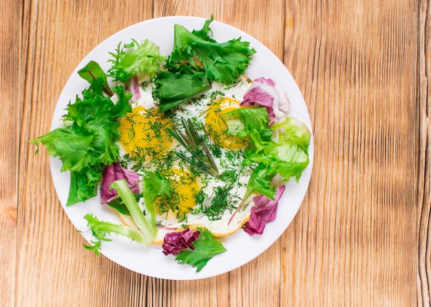 Fried eggs with greens on a plate on a wooden background Healthy breakfast