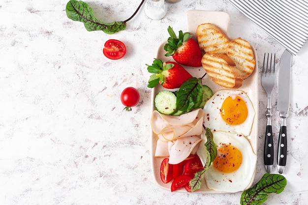 Fried eggs with ham tomatoes cucumber strawberries and toasts Delicious English Breakfast Brunch Top view overhead