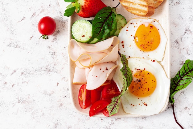 Fried eggs with ham tomatoes cucumber strawberries and toasts Delicious English Breakfast Brunch Top view overhead