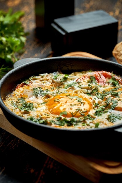 Fried eggs with tomatoes onions and pita bread in a pan on a wooden background Tasty Shakshuka