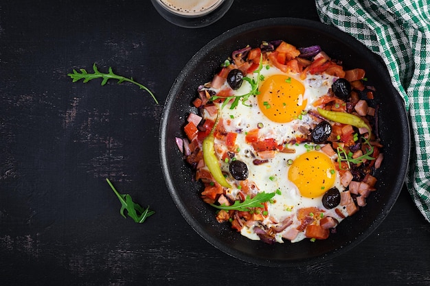 Fried eggs with vegetables on pan pepperoni tomatoes ham onion and black olives Ketogenic breakfast Top view above