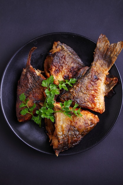 Fried fish on a black plate decorated with fresh parsley on a black background