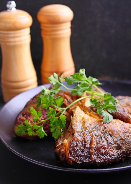 Fried fish on a black plate decorated with fresh parsley on a black background