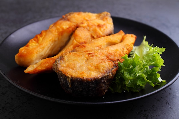 Fried fish on a black plate with lettuce