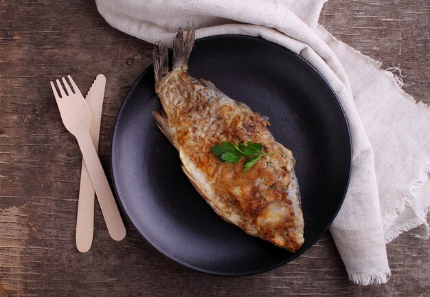 Fried fish (carp) on a black plate decorated with parsley