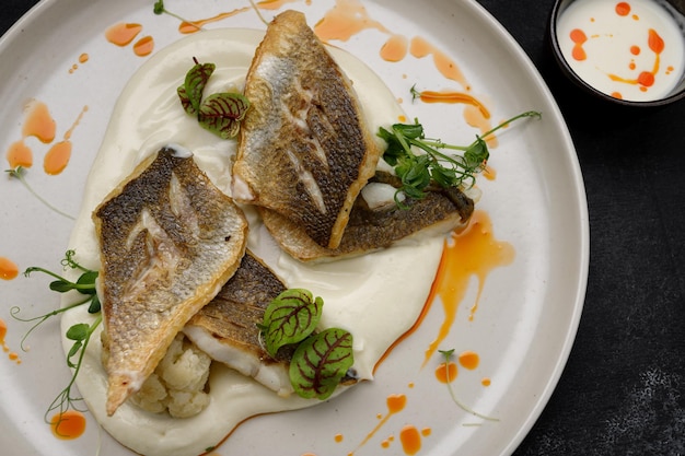 Photo fried fish fillet with sauce and herbs on a white plate