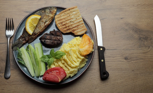 Fried fish, meat steak, and vegetables on a plate