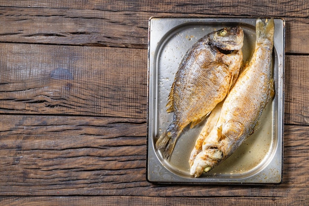 Fried fish sea bass and dorado on a metal plate on a dark wooden background rack of lamb