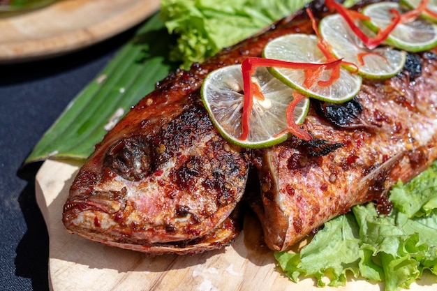 Fried fish with fresh green salad and lemon of Bali Indonesia close up Delicious roasted sea fish with lemon on wooden plate in restaurant