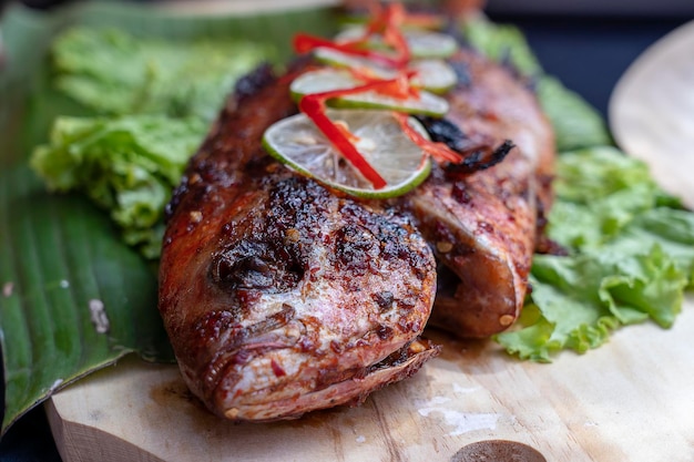 Fried fish with fresh green salad and lemon of Bali Indonesia closeup Delicious roasted sea fish with lemon on wooden plate in restaurant