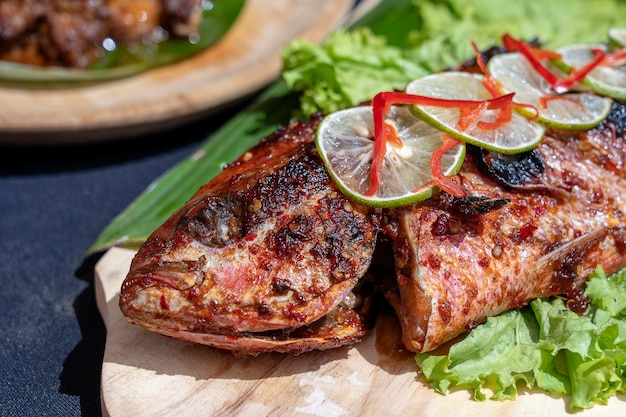 Fried fish with fresh green salad and lemon of Bali Indonesia closeup Delicious roasted sea fish with lemon on wooden plate in restaurant