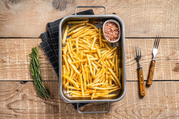 Fried French fries potatoes with salt in kitchen tray Wooden background Top view