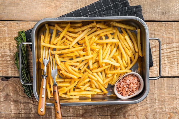 Fried French fries potatoes with salt in kitchen tray Wooden background Top view